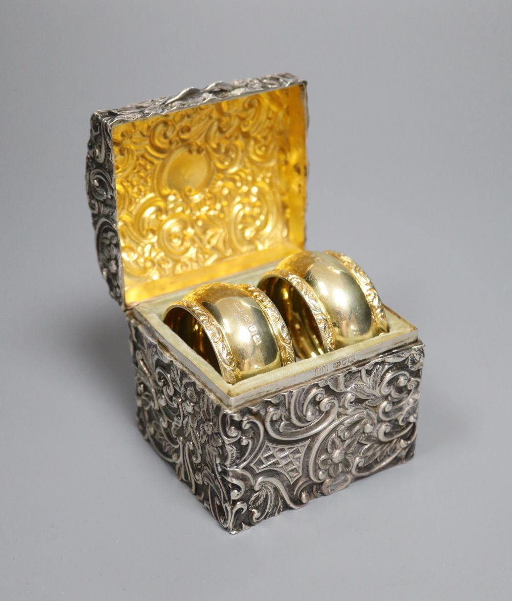 A late Victorian embossed silver serviette ring box, containing two serviette rings, Henry Matthews, Birmingham, 1892